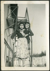 Two youth standing on steps of fire escape, one on a higher step with arms wrapped around the other