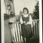 Youth holding a candle on the veranda, and another peeking out from a window holding a balloon