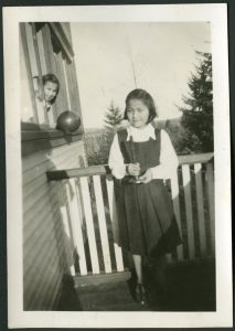 Youth holding a candle on the veranda, and another peeking out from a window holding a balloon