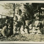Children in yard sitting on grass and playing with baby dolls