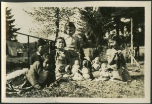 Children in yard sitting on grass and playing with baby dolls