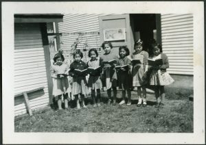 Children standing in a line between two buildings holding books which they are either reading or singing from