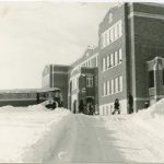 Exterior shot of Brandon Residential School with the bus in front and some children in winter.