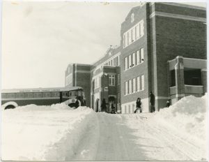 Exterior shot of Brandon Residential School with the bus in front and some children in winter.