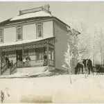 Winter scene of house with six people standing on the veranda, horse drawn sleigh to the side of the house