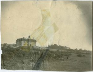 View of institution building from a distance, photograph wrinkled and taped together on the middle, caption reads 