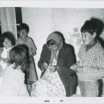 Three children standing around older adult who is holding a craft in hands