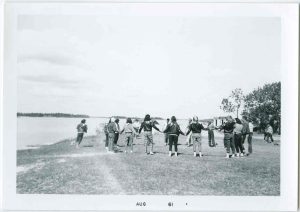 Children or youth standing holding hands in a circle by a lake.